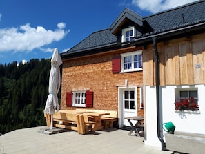 A wooden building with a tiled patio, outdoor seating, and a view of a forested area. - Holiday Home in Damuls With Swimming Pool (Damüls)
