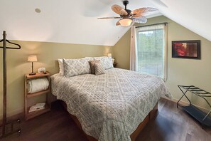 A bedroom with a sloped ceiling, a bed with patterned bedding, a bedside table with a lamp, a window with curtains, and a framed picture on the wall. - Free Ruby Falls Ticket & More-Hot Tub-Handcrafted Cabin with Tower-Lookout Mountain-Romantic Getaway (Lookout Mountain)
