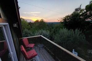 A deck with two red chairs and a small table, overlooking a forested area with a sunset view. - Free Ruby Falls Ticket & More-Hot Tub-Handcrafted Cabin with Tower-Lookout Mountain-Romantic Getaway (Lookout Mountain)