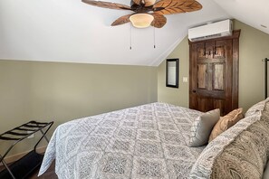 Ein Schlafzimmer mit Bett, Deckenventilator, Klimaanlage und Holztür.