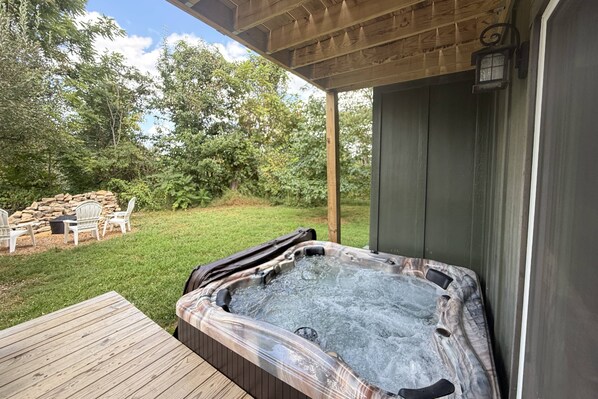 Ein Whirlpool auf einer Holzterrasse mit einer Steinwand und Stühlen im Hintergrund.