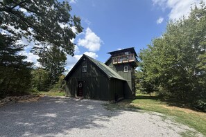 Eine zweistöckige Holzblockhütte mit Balkon, umgeben von Bäumen und einer Schotterzufahrt.