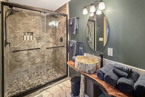 Ein Badezimmer mit einer gläsernen Duschkabine, einem hölzernen Waschtisch mit Spiegel und einer Steinwand.