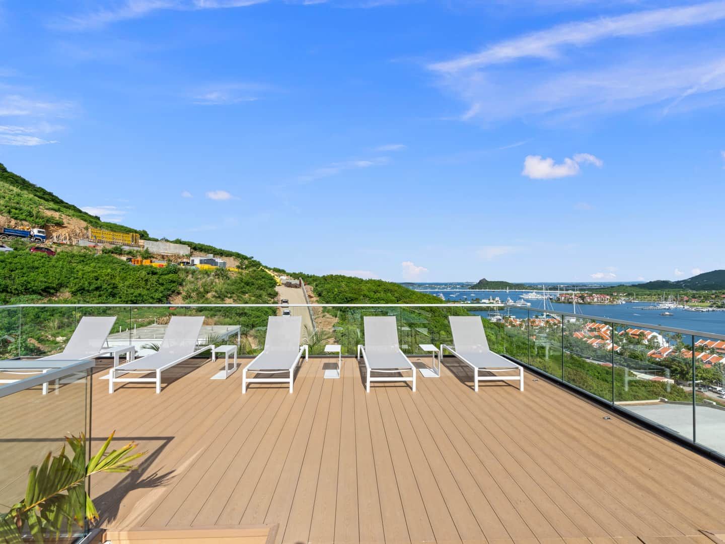 A deck with lounge chairs overlooking a marina and a hilly landscape.