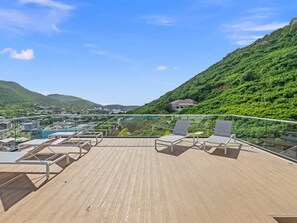 Eine Dachterrasse mit Liegestühlen und Pool mit Blick auf einen grünen Hügel und eine Stadt.