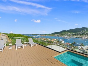 Eine Holzterrasse mit Liegestühlen und einem Pool mit Blick auf eine Marina und eine Skyline.