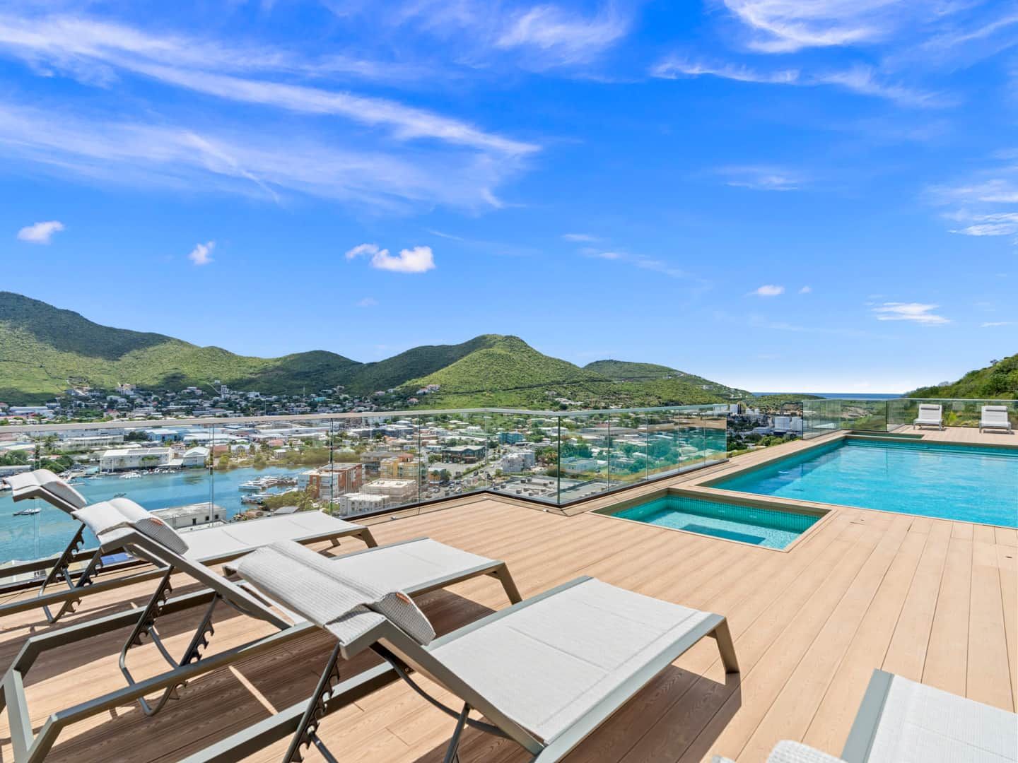 A rooftop pool area with lounge chairs and a view of a coastal town and hills.