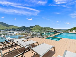 A rooftop pool area with lounge chairs and a view of a coastal town and hills. - C303 - Beautiful 1 Bedroom with Terrace (Cole Bay)