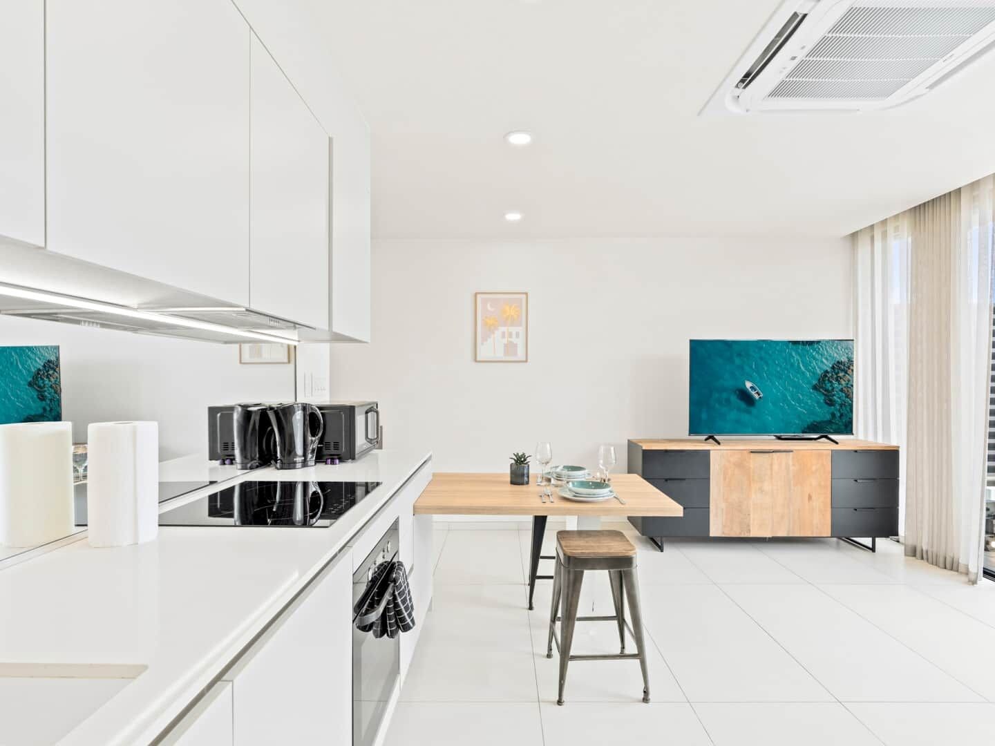 A modern kitchen with a central island, a dining area, and a TV mounted on the wall.