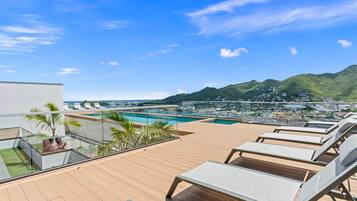 Ein Poolbereich auf dem Dach mit Liegestühlen und Blick auf das Meer und die Berge.