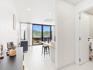 A modern living room with a large window, a flat-screen TV, and a dining area with a view of the hills. - C303 - Beautiful 1 Bedroom with Terrace (Cole Bay)