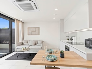 A modern kitchen with white cabinetry, a dining table set for two, and a sofa in the adjacent living area. - C303 - Beautiful 1 Bedroom with Terrace (Cole Bay)