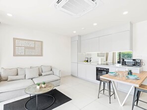 A modern kitchen with white cabinets, a dining area with a wooden table and bar stools, a sofa with cushions, and a black rug. - C303 - Beautiful 1 Bedroom with Terrace (Cole Bay)