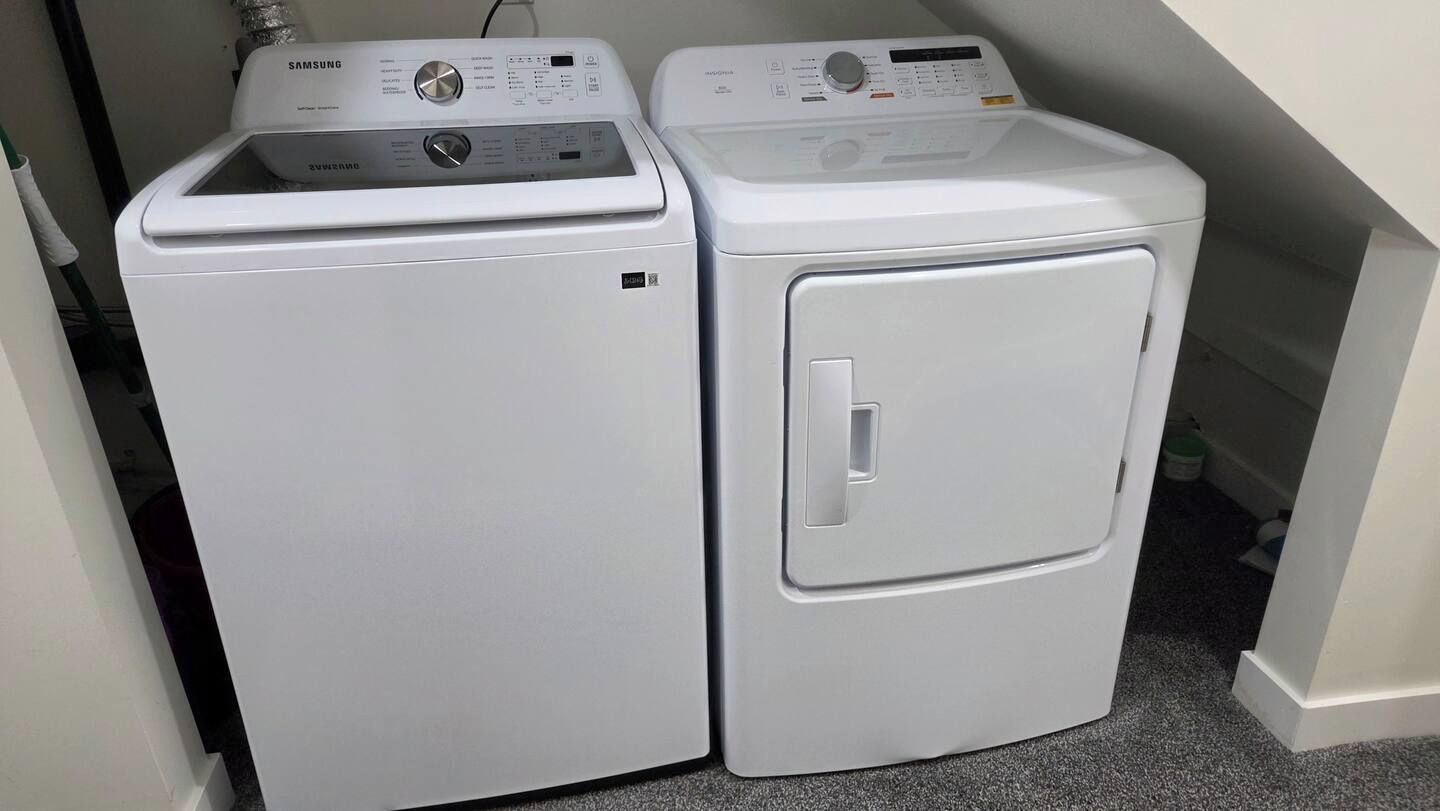 Deux machines à laver à chargement frontal, de couleur blanche, se trouvent dans une buanderie dont le sol est carrelé.