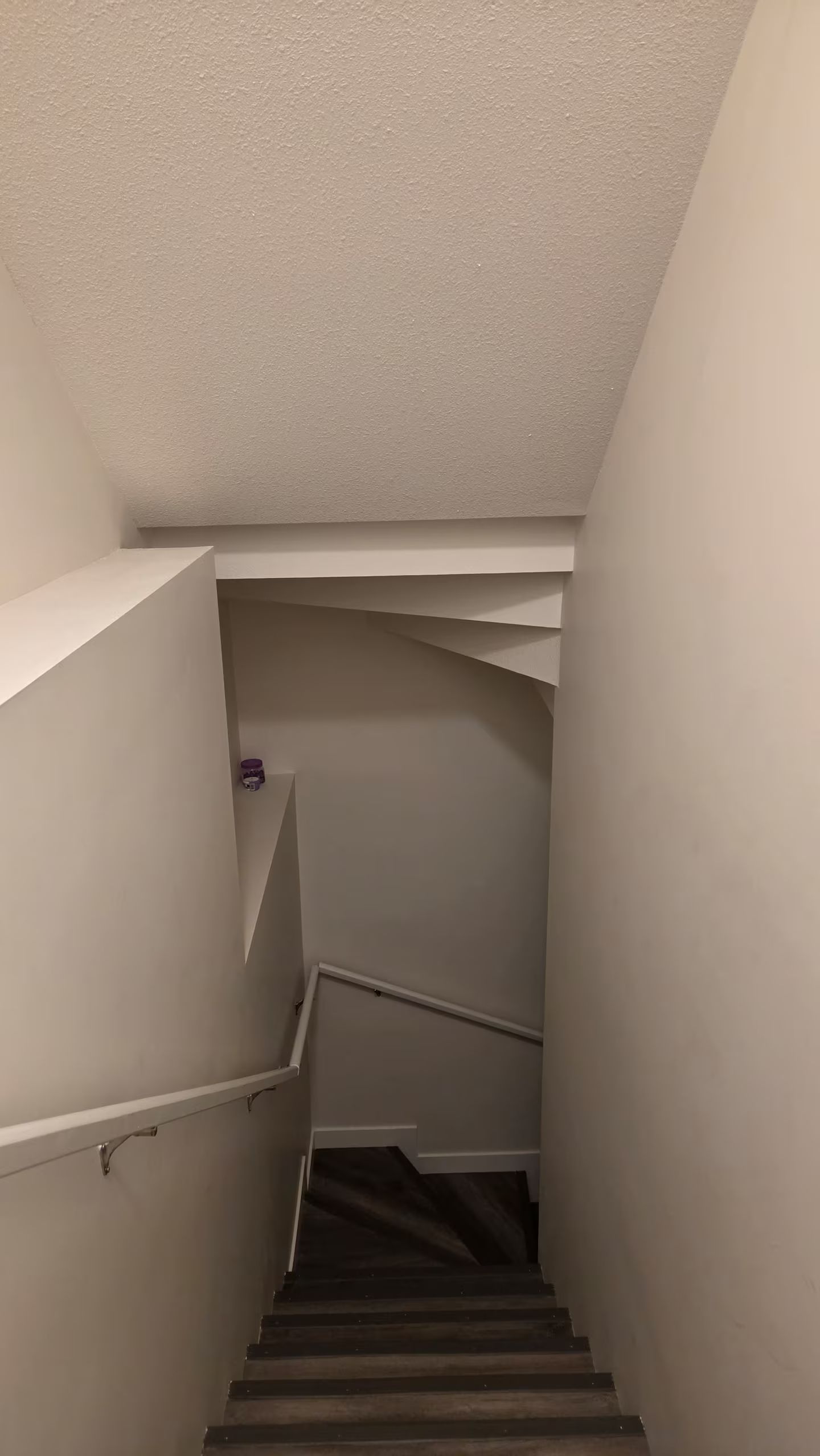 Eine schmale Treppe mit Handlauf, die zu einer Zwischenebene führt, auf der sich ein kleines Objekt an der Wand befindet.
