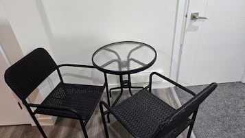 Une petite pièce avec une porte blanche, une table ronde en verre et deux chaises noires.