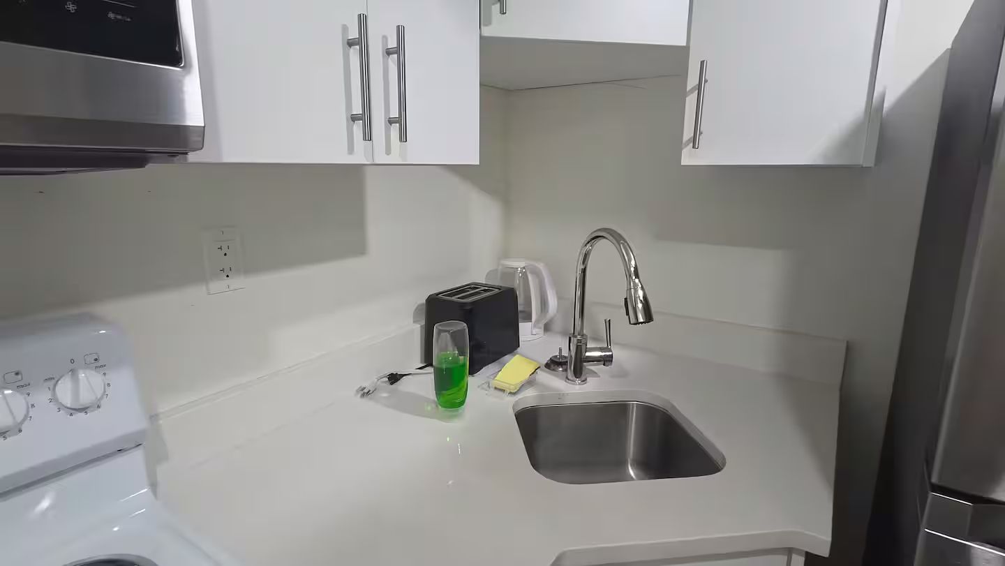 A kitchen with white cabinets, a stainless steel sink, a toaster, and a green bottle.