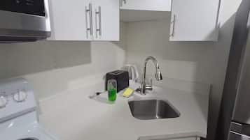 A kitchen with white cabinets, a stainless steel sink, a toaster, and a green bottle.