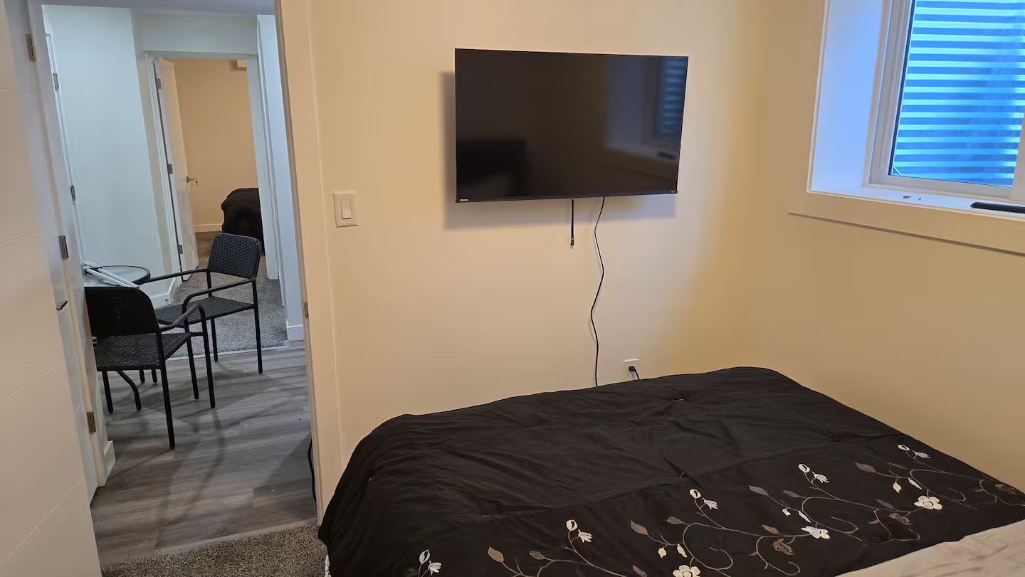 Ein Schlafzimmer mit einem Bett, einem an der Wand befestigten Fernseher und einem Fenster mit Jalousien.