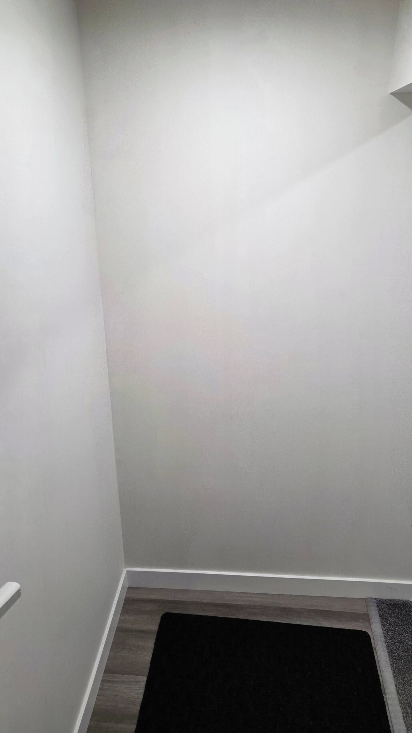 Un coin de pièce avec un mur blanc et un tapis de sol foncé.