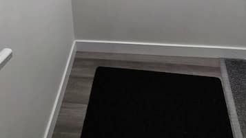 Un coin de pièce avec un mur blanc et un tapis de sol foncé.