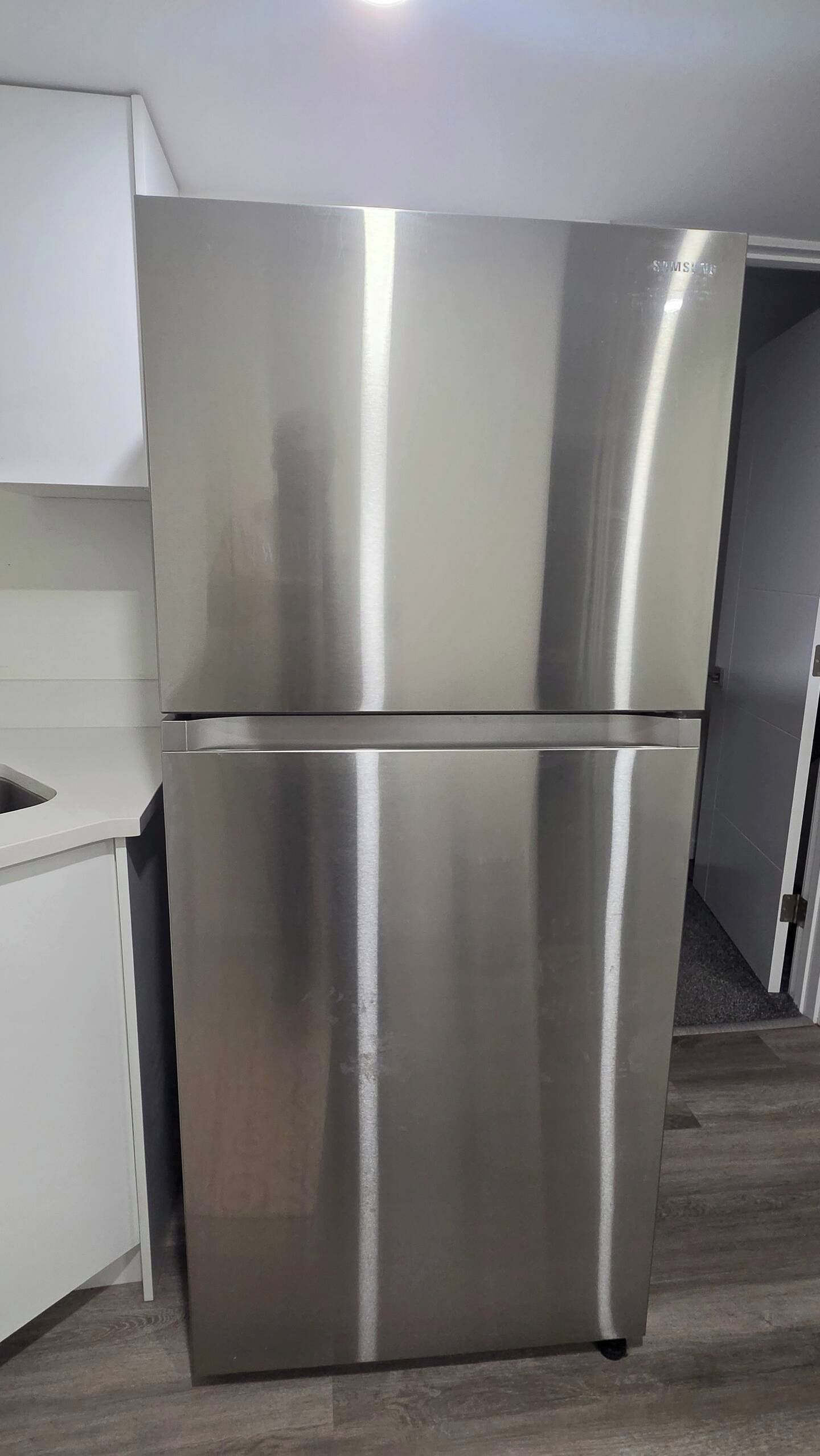 A stainless steel refrigerator in a kitchen with a white countertop and a grey floor.