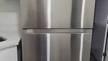 A stainless steel refrigerator in a kitchen with a white countertop and a grey floor.