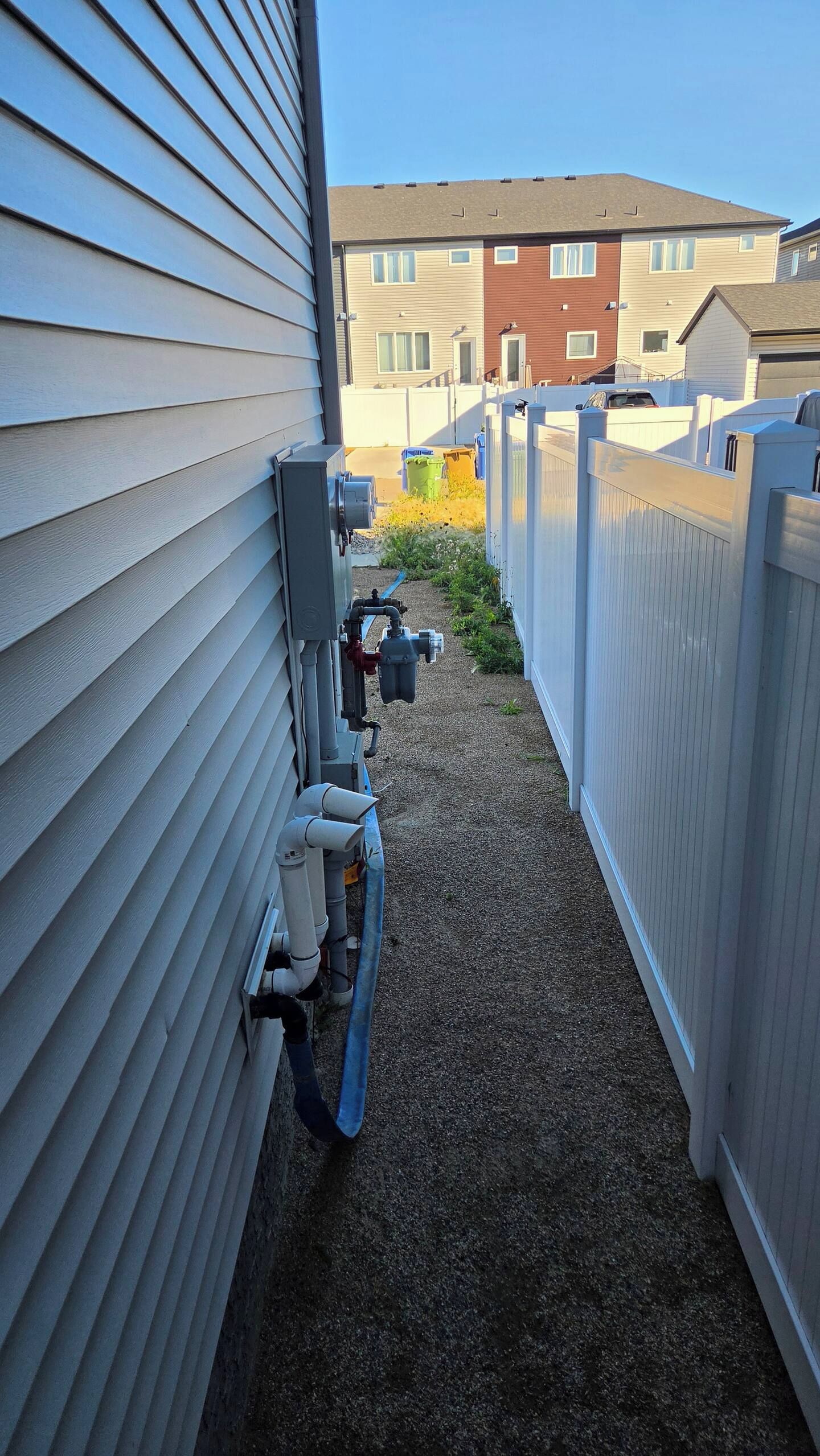 A narrow gravel path flanked by a white fence and a building with siding.