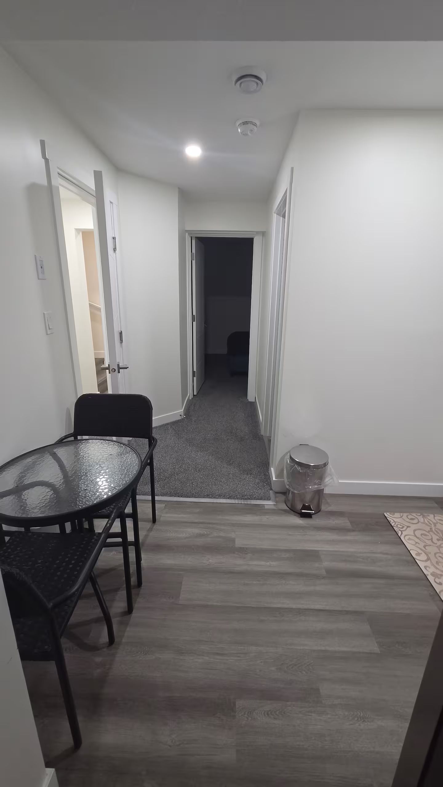 Een gang met een eettafel en stoelen, een prullenbak en een deur naar een andere kamer.