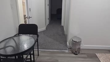 Een gang met een eettafel en stoelen, een prullenbak en een deur naar een andere kamer.