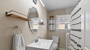 Casa de banho com lavatório branco, espelho e sanita. Há um porta-toalhas com uma toalha pendurada.