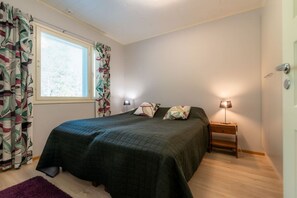 Um quarto com cama, duas luminárias de cabeceira, uma janela com cortinas e uma porta.
