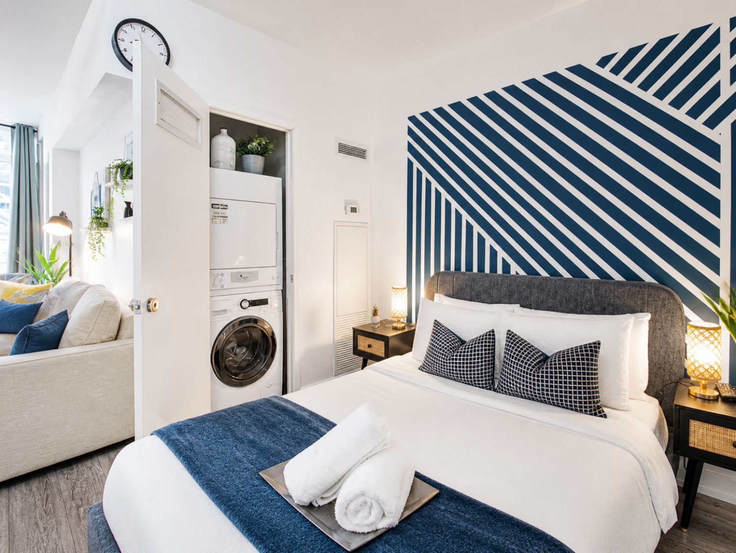 Habitación de hotel con cama, lavadora, mesita de noche y pared con diseño a rayas.