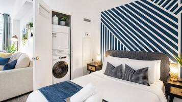 Habitación de hotel con cama, lavadora, mesita de noche y pared con diseño a rayas.