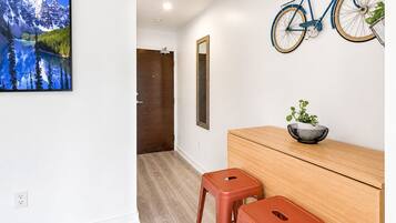 A room with a wooden desk, two stools, a bicycle mounted on the wall, a framed picture, and a door leading to another room.