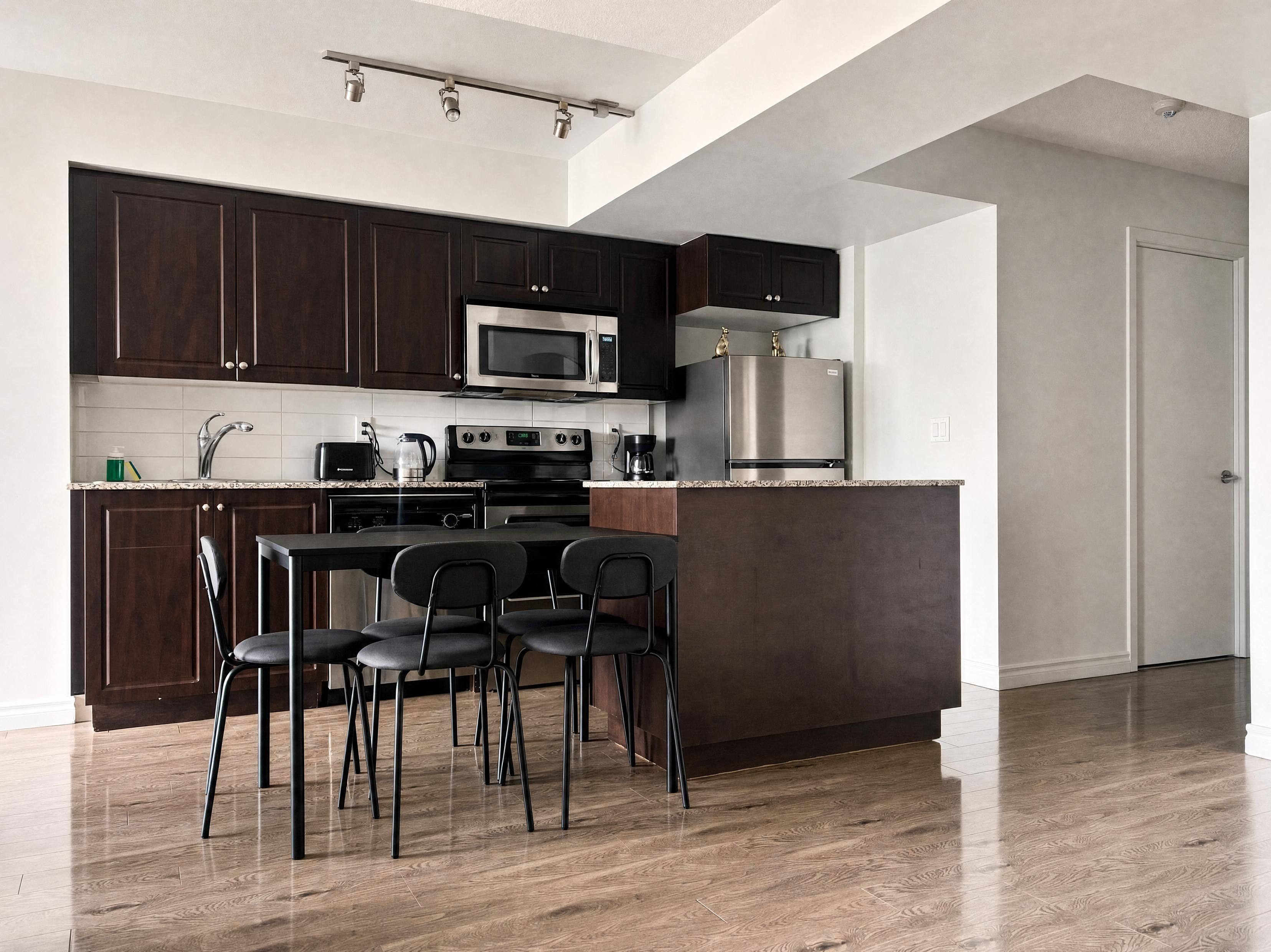 A modern kitchen with dark wood cabinets, stainless steel appliances, and a dining area with four chairs.