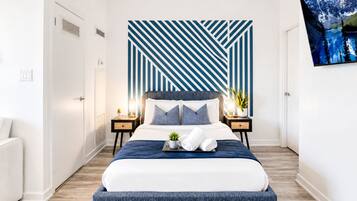 A modern bedroom with a large bed, a geometric wall design, a flat-screen TV, and a potted plant.