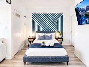 Un dormitorio moderno con una cama grande, un diseño geométrico en la pared, un televisor de pantalla plana y una planta en maceta.