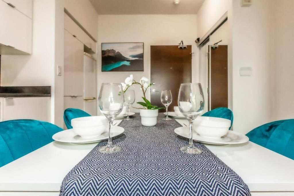 A dining area with a table set for two, a potted plant, and a painting on the wall.