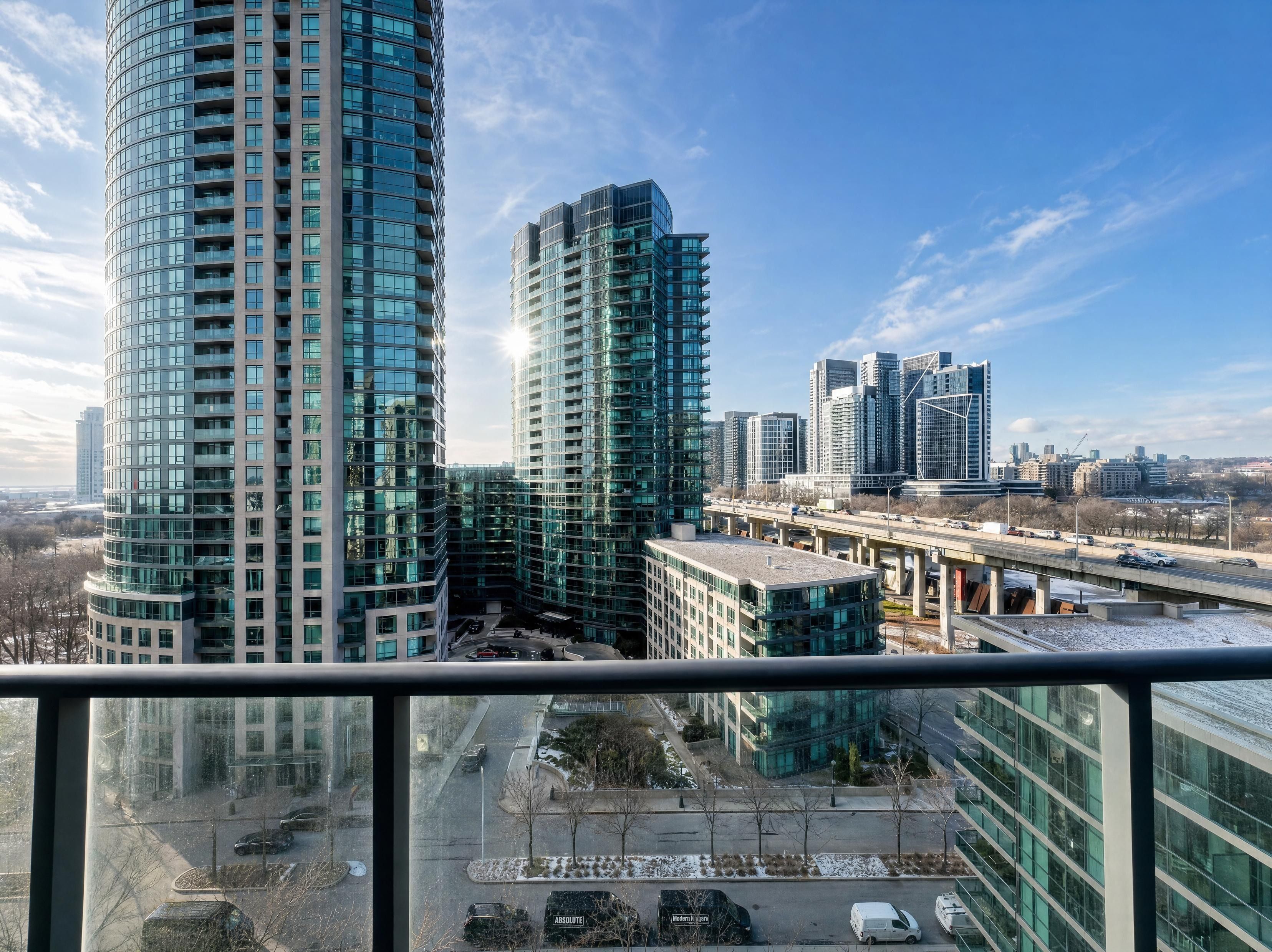 A high-rise building with a curved facade, a parking area with several cars, and a clear sky.