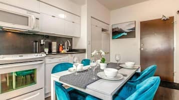 Una cocina moderna con electrodomésticos blancos, una mesa de comedor con sillas azules y un cuadro en la pared.