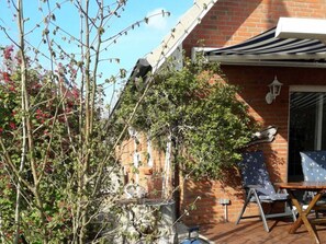 Ein Backsteinhaus mit überdachter Terrasse, einem Metallstuhl und einem Tisch.