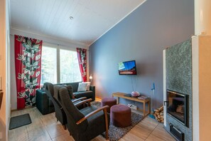 Una sala de estar con sofá, sillas, televisor, chimenea y ventana con cortinas.