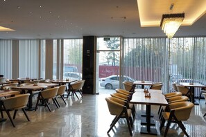 A modern dining area with tables and chairs, large windows, and a chandelier. - New My World Hotel (Istanbul)