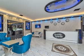 A modern lobby with a reception desk, seating area, and decorative elements like clocks and a patterned rug. - New My World Hotel (Istanbul)