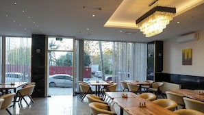 A restaurant with a modern interior, featuring wooden tables and chairs, a chandelier, and large windows offering a view of the street. - New My World Hotel (Istanbul)