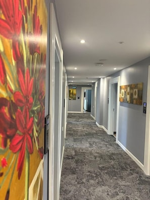 A hotel hallway with a carpeted floor, doors on the right, and artwork on the walls. - New My World Hotel (Istanbul)