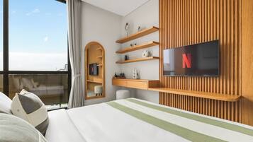 A modern hotel room with a large bed, a television mounted on the wall, wooden shelving, and a window with curtains.