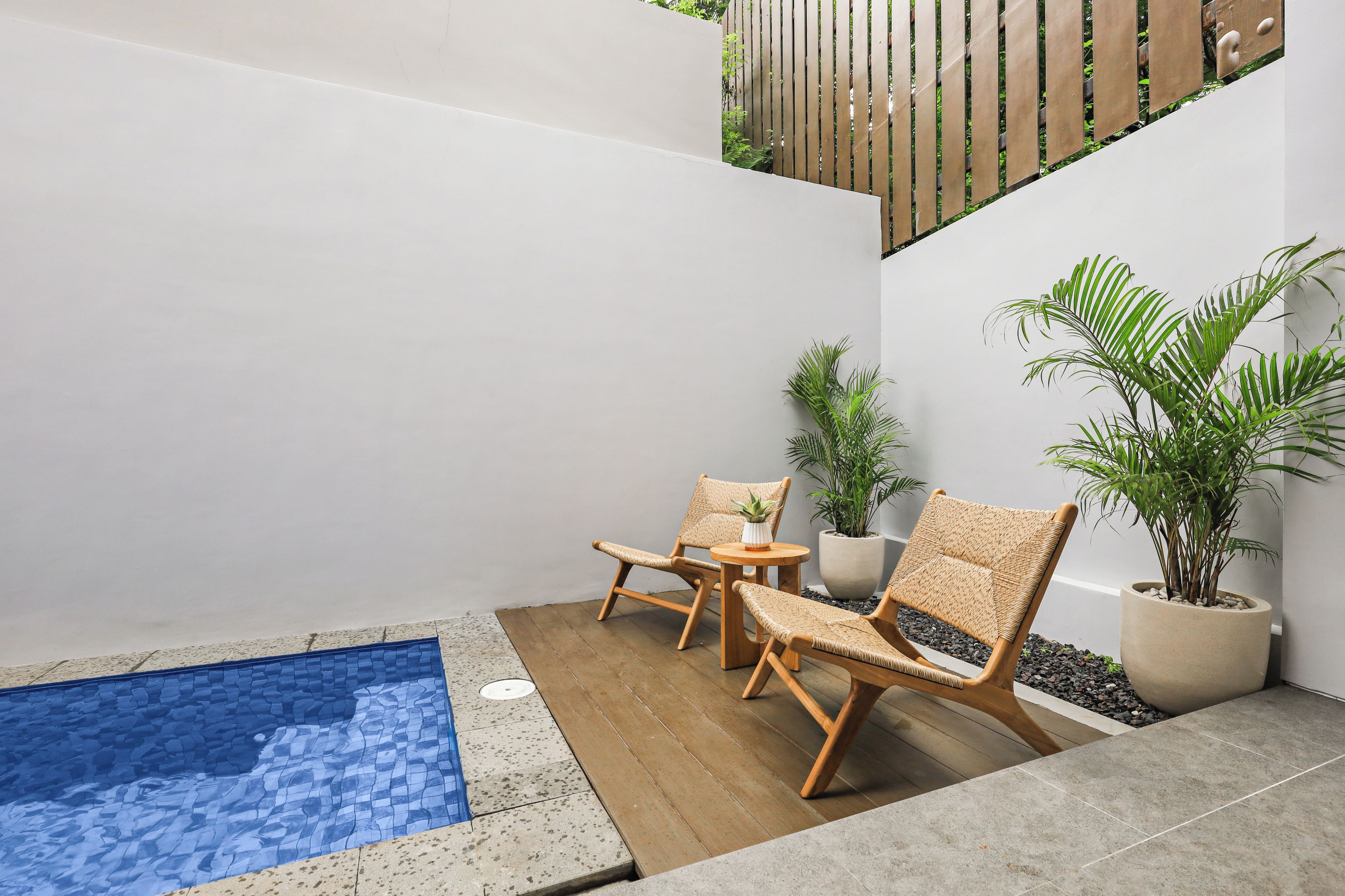 A small outdoor pool area with two wicker lounge chairs and a potted plant.