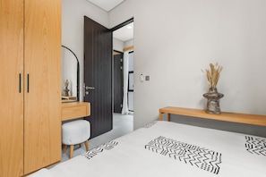 A modern bedroom with a wooden wardrobe, a bedside table with a vase, and a bed with a geometric-patterned bedspread.